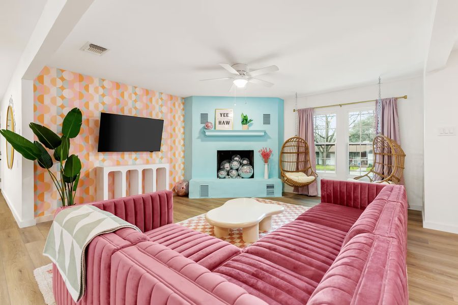 The same living room after: geometric wallpaper, a teal fireplace and pink velvet sofas.