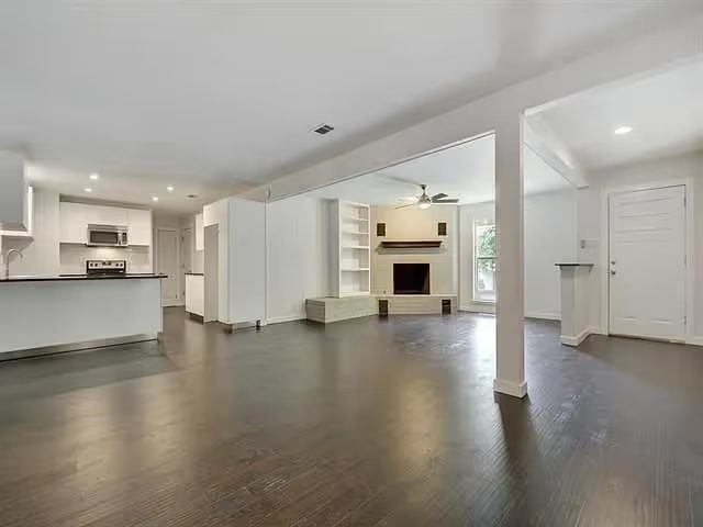 The living room before renovation: empty, bare white walls and dark floors.